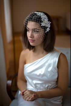 a woman in a white dress wearing a veil with flowers on it's head