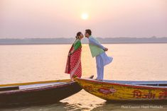 two people standing on top of boats in the water at sunset or dawn, with one person holding his arm around the other's neck