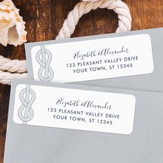 two gray envelopes with rope and address labels on them sitting on a wooden table