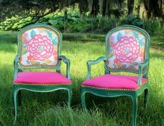 two green chairs sitting in the grass with pink cushions on top of them and one has a flower design on it