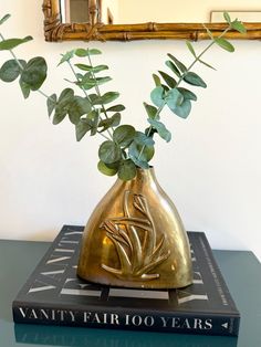 a gold vase with some green leaves in it on a table next to a mirror