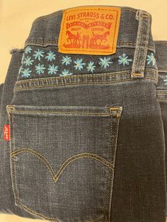 "These Levi's are uniquely embroidered with a medium blue and cream colored daisies. The style is \"shaping skinny\" with frayed bottoms. Although the jeans are not new they are in perfect condition.  Waist: 28 inches  Length: 26 inches  Style: shaping skinny with frayed bottoms  Wash: dark  Fly: Zip" Embroidered Dark Wash Mid-rise Bottoms, Embroidered Mid-rise Dark Wash Bottoms, Fitted Embroidered Dark Wash Jeans, Fitted Dark Wash Embroidered Jeans, Colored Daisies, Bill Blass Jeans, Hot Cold Packs, Bill Blass, Cold Pack