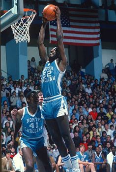 two men playing basketball in front of an arena full of people and one man is jumping up to dunk the ball