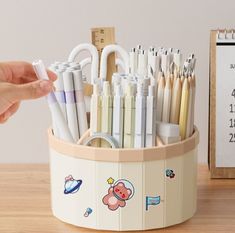 a pen holder filled with pens and pencils next to a calendar on a table