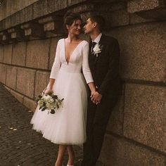 a bride and groom leaning against a stone wall