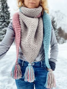 a woman is standing in the snow wearing a scarf with tassels on it