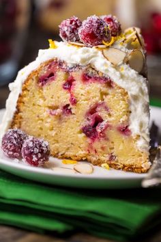 a piece of cake with white frosting and cranberries sits on a plate