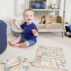 a toddler sitting on the floor playing with wooden letters and puzzles in front of him