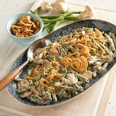 an oval serving dish filled with green beans, mushrooms and onions next to a bowl of onion rings