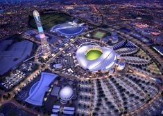 an aerial view of a stadium at night with lights on the ground and buildings in the background