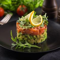 a black plate topped with an avocado and tomato salad on top of lettuce