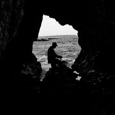 a man sitting on top of a rock next to the ocean