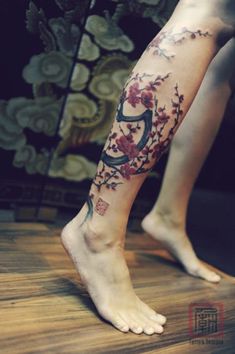 a woman's legs with flowers and numbers tattooed on her left leg, in front of a plant