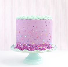 a purple cake with sprinkles and pink frosting on a white pedestal