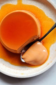 a spoon full of caramel sauce on a white plate with orange liquid in it