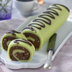 there is a chocolate roll with green icing on the white plate next to a knife