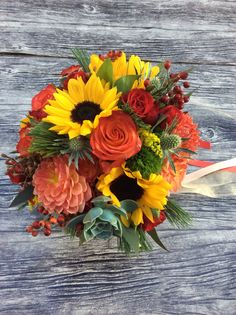 a bouquet of sunflowers, roses and other flowers on a wooden table with ribbon