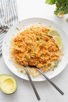 a white plate topped with chicken and rice next to an avocado