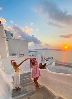 two women in white dresses standing on steps next to the ocean with their arms around each other