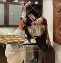 two women in the kitchen with some muffins on a tray and one holding a pan