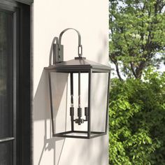 an outdoor light hanging on the side of a building with trees in the back ground