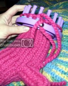 a hand holding a pink and purple object on top of a colorful bed spread with multicolored crochet