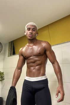 a man with white hair and no shirt standing in a bathroom next to a fan