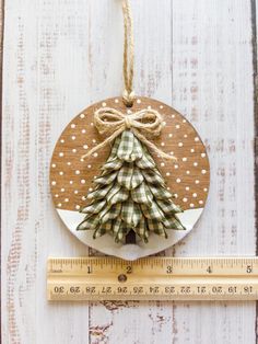 a wooden ornament with a christmas tree on it next to a measuring tape