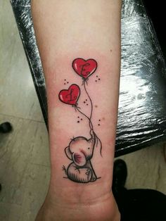 a person with a tattoo on their arm holding two heart shaped balloons in the shape of a bear