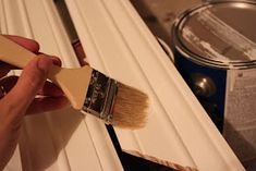 a person is holding a paintbrush and painting the side of a white window frame