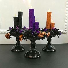 three black candles with purple and orange flowers in them