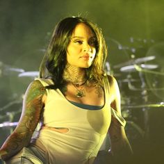 a woman with tattoos standing in front of a drum set on stage at a concert