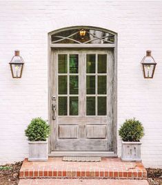 a white brick building with two potted plants on the steps and a wooden door