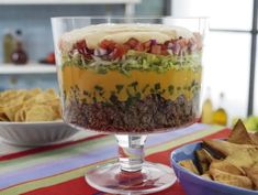 a layered salad with tortilla chips and salsa in a glass dish on a table