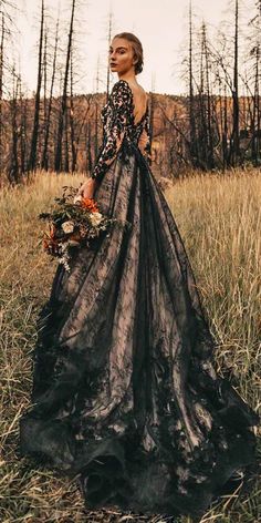 a woman standing in a field wearing a long black dress with sheer sleeves and an open back