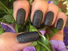 a woman's hand with black nail polish on it and purple flowers in the background