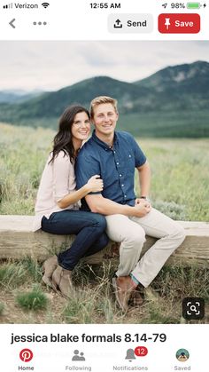 a man and woman sitting on a wooden bench in the grass with mountains in the background