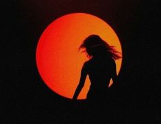 the silhouette of a woman in front of an orange sun with her hair blowing in the wind