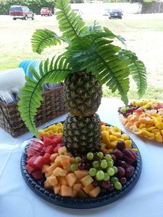 a platter filled with fruit and a pineapple on top of a table next to a palm tree