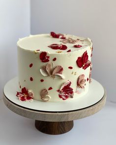 a white cake with red and pink flowers on it sitting on top of a wooden stand