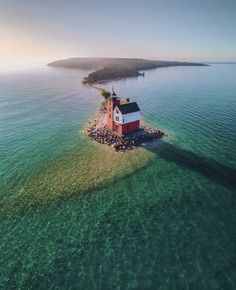 an island with a small house on it in the middle of the ocean, surrounded by water