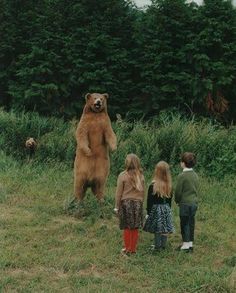 three children standing in front of a large brown bear