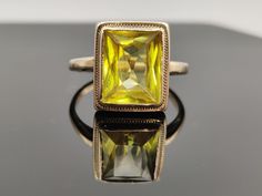 A uniquely faceted retro travel ring. It was made as a safe travel piece , while the real yellow saphire or diamond ring set in 18k remained  under lock and key.  The rectagular stone has a fancy cut and is bezel set in gold with a fine gold braid wrapping the setting beautifully.  The travel pieces were usually set in 8 or 9kt in UK and 10k in the US. The shank on this ring shows no stamp.  Am pricing it as gold filled   Very Good Vintage Condition  please view photos carefully  approx. size 4. Gold Rectangular Sapphire Ring For Formal Occasions, Yellow Rectangular Ring As A Gift, Gold Sapphire Ring With Rectangular Shape For Formal Events, Rectangular Sapphire Ring In Gold For Formal Occasions, Yellow Square Cut Rings For Gift, Yellow Rectangular Ring For Gift, Yellow Rectangular Rings For Gift, Yellow Rectangular Anniversary Ring, Vintage Rectangular Emerald Ring Gift