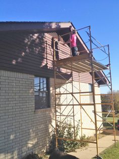 a woman standing on top of a scaffold next to a black dog in front of a house