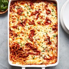 a white casserole dish filled with pasta and sauce, garnished with parsley