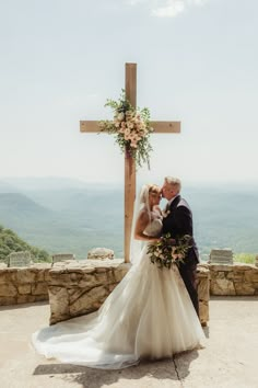 a bride and groom standing in front of a cross at the top of a mountain