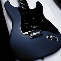 a black electric guitar sitting on top of a white sheet