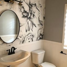 a white toilet sitting next to a sink in a bathroom under a mirror with flowers on it