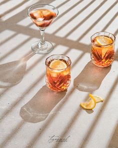 three glasses filled with drinks sitting on top of a white table next to lemon wedges