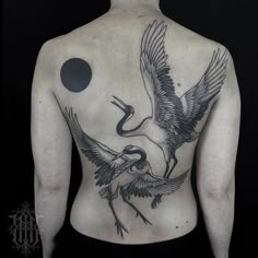 the back of a man with a bird and moon tattoo on his upper half body